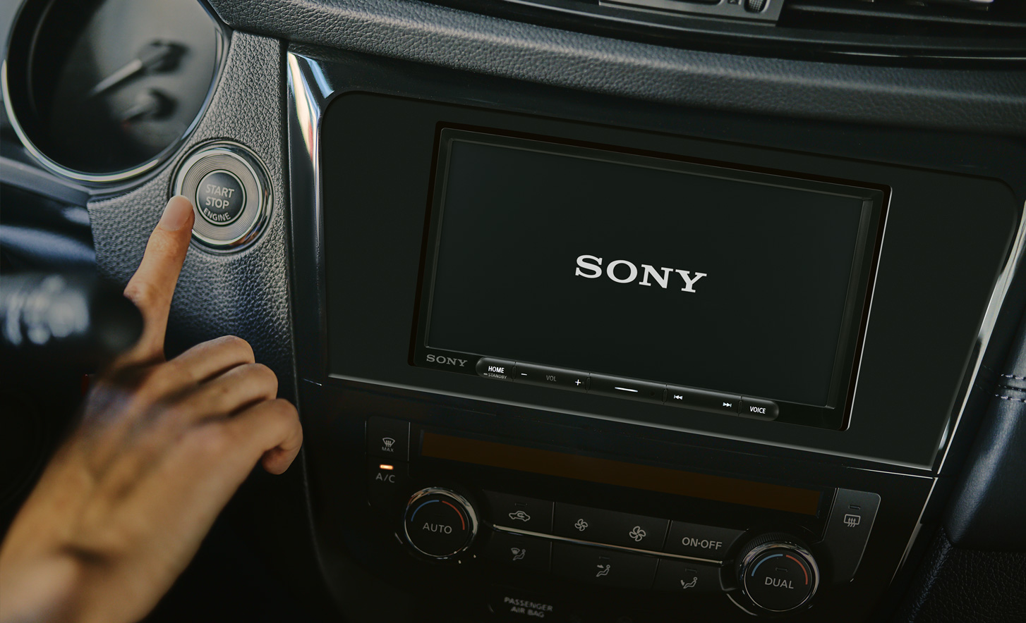 Front view of the XAV-AX3700 digital multimedia receiver installed on a car dashboard with a finger pressing the ignition button.