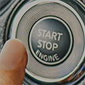 A finger about to press the ignition button of a car.